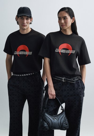 Zwarte t-shirts met een rood halvemaanlogo en de tekst "MARINESERRE", gecombineerd met zwarte broek met patroon en een gestructureerde zwarte handtas.