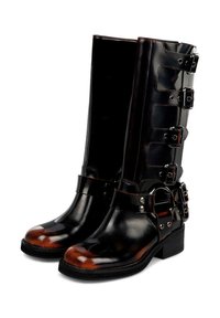 Par de botas de cuero negras y marrones hasta la mitad de la pantorrilla con tacones gruesos, correas decorativas y múltiples hebillas plateadas en los laterales.