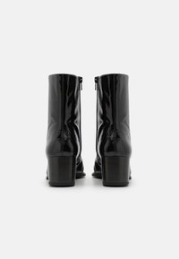 Botine negre din piele patentată, cu textură netedă, închidere cu fermoar la spate și design cu toc bloc.