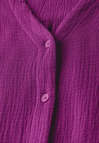 Chemise à boutons violette vibrante en tissu texturé, avec un décolleté en V et deux boutons violets superposés à l'avant.