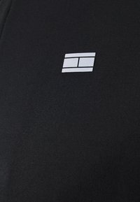 Un tessuto nero dalla consistenza liscia presenta un logo rettangolare bianco al centro, posizionato in modo rilevante sulla superficie dell'abbigliamento.
