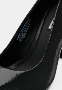 Pantofii din piele patent neagră, cu vârful rotunjit și un finisaj neted, lucios. Interiorul prezintă eticheta cu detalii despre mărimea și originea fabricației.
