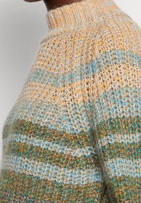 Sweter dzianinowy z wysokim dekoltem. Projekt zawiera paski w odcieniach pomarańczowym, turkusowym i ziemistych, o miękkiej teksturze.