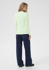 Camicia a maniche lunghe di colore verde chiaro con righe bianche, abbinata a jeans a gamba ampia blu. Tessuto in cotone con una consistenza liscia e vestibilità classica.