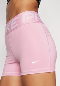 Pink athletic shorts made of stretch fabric with a wide waistband featuring "NIKE" in light pink and a white Nike logo on the side.
