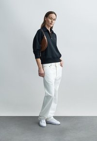 Fekete cipzáras pulóver, fehér bőszárú farmer és fehér tornacipő. Barna válltáska, minimalista design, nincs látható minta.