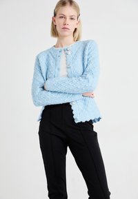 Light blue knitted cardigan with a textured diamond pattern, scalloped hem, and three decorative buttons down the front.