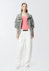 Lagani sivi jakna s teksturiranim uzorkom, ružičasti top bez rukava, bijele široke hlače i bijele ravne cipele s svijetlim naglascima.