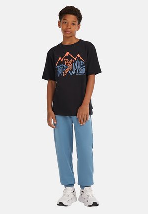 Camiseta de algodón negra con un gráfico colorido que presenta montañas y texto. Pantalones de chándal azul claro y zapatillas blancas complementan el atuendo.
