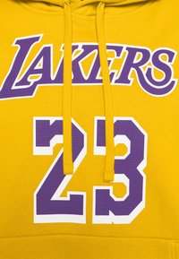 Sweat à capuche jaune avec "LAKERS" en lettres cursives violettes et "23" en texte gras violet et blanc, avec des cordons assortis et une texture identique.