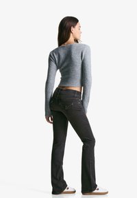 Gray cropped sweater with ribbed hem, paired with dark flared jeans and white shoes. The outfit features long sleeves and a simple design.