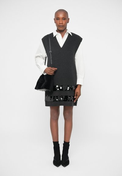 Top negro sin mangas de punto sobre una camisa blanca de botones, combinado con una falda negra con lentejuelas. Accesorios incluyen un bolso negro y zapatos de tacón.