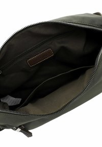 Interno di una borsa in tessuto verde oliva con una tasca con zip, dotata di un'etichetta in pelle marrone. Texture liscia e forma arrotondata.