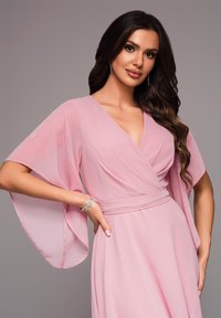 Rosa omslagklänning gjord av mjukt, flödande tyg med vida ärmar och en djup V-ringning; inkluderar ett dekorativt midjeband och en armbandsaccent.