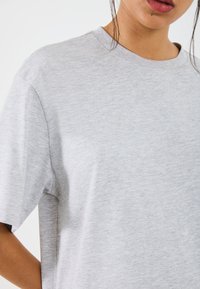 Light grey short-sleeve T-shirt in soft, textured fabric. Features a round neckline and a relaxed fit with dropped shoulders.