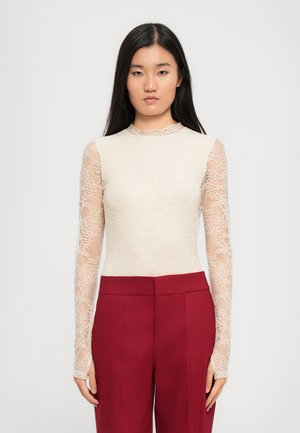 Long-sleeve bodysuit features a nude lace overlay with floral patterns and a scalloped neckline, paired with fitted burgundy trousers.