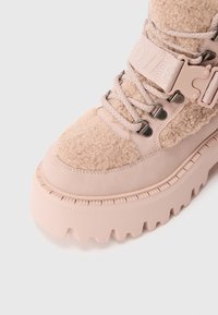 Gruby różowy zimowy but z panelami z polaru, grubą, rowkowaną podeszwą, sznurowaniem z przodu oraz szerokim paskiem z klamrą do zapięcia.