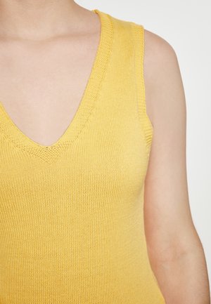 Gul strikket ærmeløs top med dyb V-hals. Har et struktureret mønster og en blød finish. Stoffet fremstår let og åndbart.