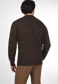 Brauner Strickpullover mit strukturierter Oberfläche, runder Ausschnitt und langen Ärmeln, kombiniert mit beigen Hosen.