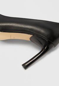 Czarny skórzany but na wysokim obcasie z zaostrzonym noskiem i eleganckim designem. Obcas jest wąski, ma około 10 cm wysokości i gładkie wykończenie.