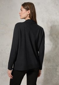 Cardigan nero in maglia con colletto e polsi a costine. Presenta una vestibilità rilassata e spacco laterale. Texture liscia su uno sfondo testurizzato.