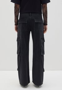 Pantalones cargo negros de corte holgado, con múltiples bolsillos de parche en los laterales y la parte trasera, hechos de una tela de mezclilla texturizada.