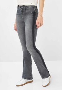 I jeans a zampa d'elefante in denim grigio presentano un aspetto sbiadito con un pannello laterale più scuro. Sono dotati di una zip frontale standard e tasche, abbinati a sneakers bianche.