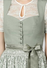 Green polka dot dress with a fitted bodice, decorative buttons, and a bow at the waist. The skirt features a floral pattern and smocked texture.