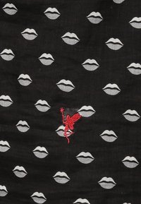 Tissu noir avec des impressions argentées de lèvres répétées et une figure brodée rouge, présentant un design distinct et une texture lisse.