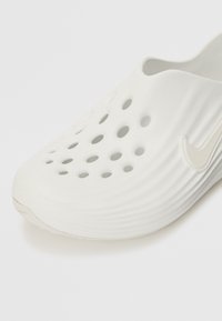 Scarpa bianca slip-on realizzata in gomma testurizzata, con numerosi fori di ventilazione e un logo goffrato discreto sul lato.