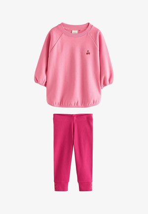 Pinkes Langarmshirt mit kleinem Kirsch-Stickerei, kombiniert mit gerippten, dunkelrosa Leggings mit Knopfdetails an den Ärmelbündchen.