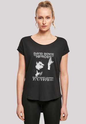 Schwarzes T-Shirt mit kurzen Ärmeln, das einen grafischen Druck von David Bowie zeigt, mit dem Text "‘Heroes’" und Konzertdetails von Earl's Court, London, 1978.