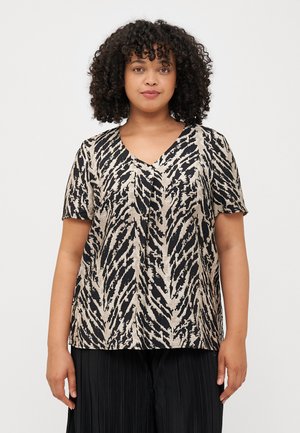 En kvinne med krøllete hår modellerer en kortermet V-hals topp med et dristig, svart-og-beige dyretrykk, kombinert med svarte plissert bukser.
