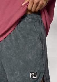 Γκρι, υφασμάτινες βερμούδες με πλευρικές τσέπες και μαύρο έμβλημα Nike. Μερικώ ς καλυμμένες από ροζ μπλούζα, που αποπνέει casual στυλ.