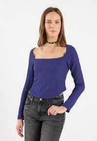 Maglia a maniche lunghe viola a coste con scollo quadrato, abbinata a jeans neri. Tessuto texture con design aderente e orlo dritto.