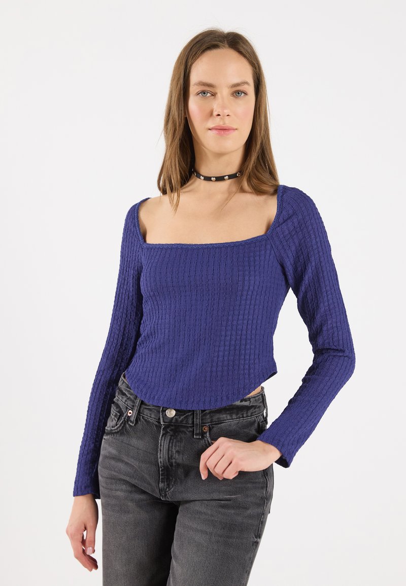 Maglia a maniche lunghe viola a coste con scollo quadrato, abbinata a jeans neri. Tessuto texture con design aderente e orlo dritto.