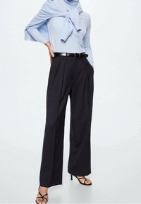 Blue long-sleeve top with bow detail, black pinstriped wide-leg trousers, shiny black belt, and open-toed black heels.
