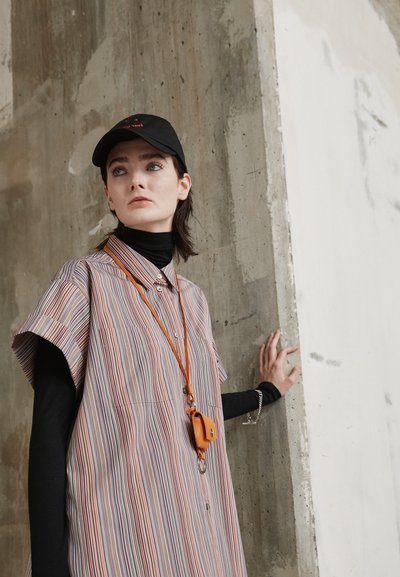 Vestido camisola às riscas em cores pastel, mangas curtas, frente com botões, combinado com um suéter de gola alta preto e uma boina preta; inclui um estojo de acessórios laranja.