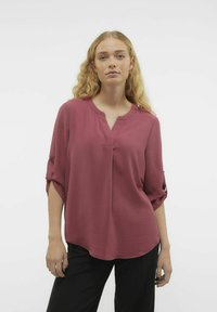 Top svasato a maniche corte in un profondo rosa con un tessuto testurizzato, scollatura a V e maniche arrotolate con bottone. Abbinato a pantaloni scuri.
