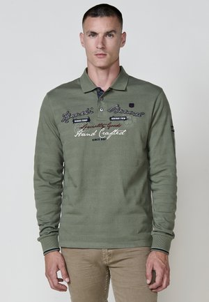 Camisa polo de manga larga en verde oliva con tejido texturizado. Presenta detalles de logo bordado y un cuello y puños en contraste de color navy.