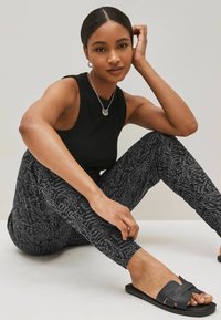 Zwarte geribbelde tanktop, gestreepte zwarte leggings met grijs abstract ontwerp en zwarte platte sandalen met strikdetail.