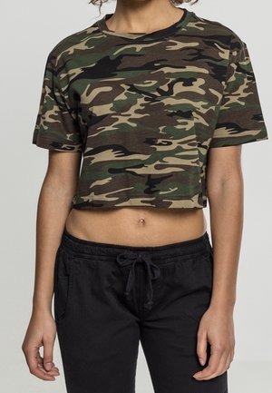 Person trägt ein grünes und braunes Tarnmuster-Cropped-T-Shirt und schwarze Hosen mit Kordelzug, gezeigt von Hals bis Hüfte.