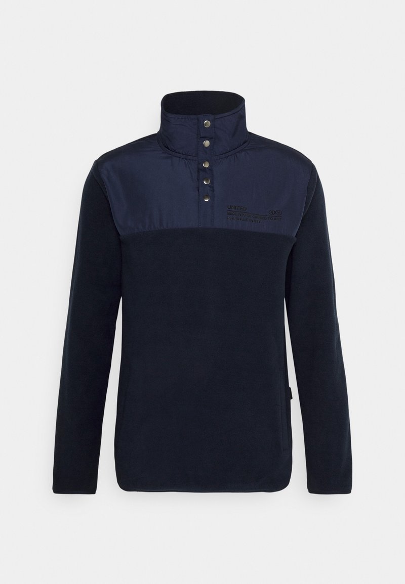 Marineblauer Fleecepullover mit hohem Kragen, der ein kontrastierendes Oberteil, Druckknöpfe und ein aufgedrucktes Logodetail auf der Brust aufweist.