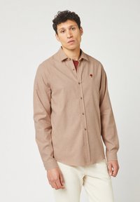 Camicia a righe in tessuto beige e marrone chiaro, con taschino sul petto con un design ricamato. Maniche lunghe e vestibilità rilassata.