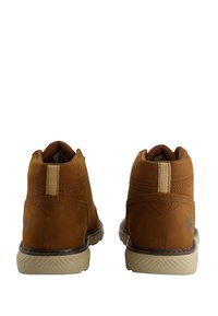 Botas de ante marrón hasta el tobillo con suela de goma beige, forro textil, detalles de costura y un pequeño logo en el talón exterior.