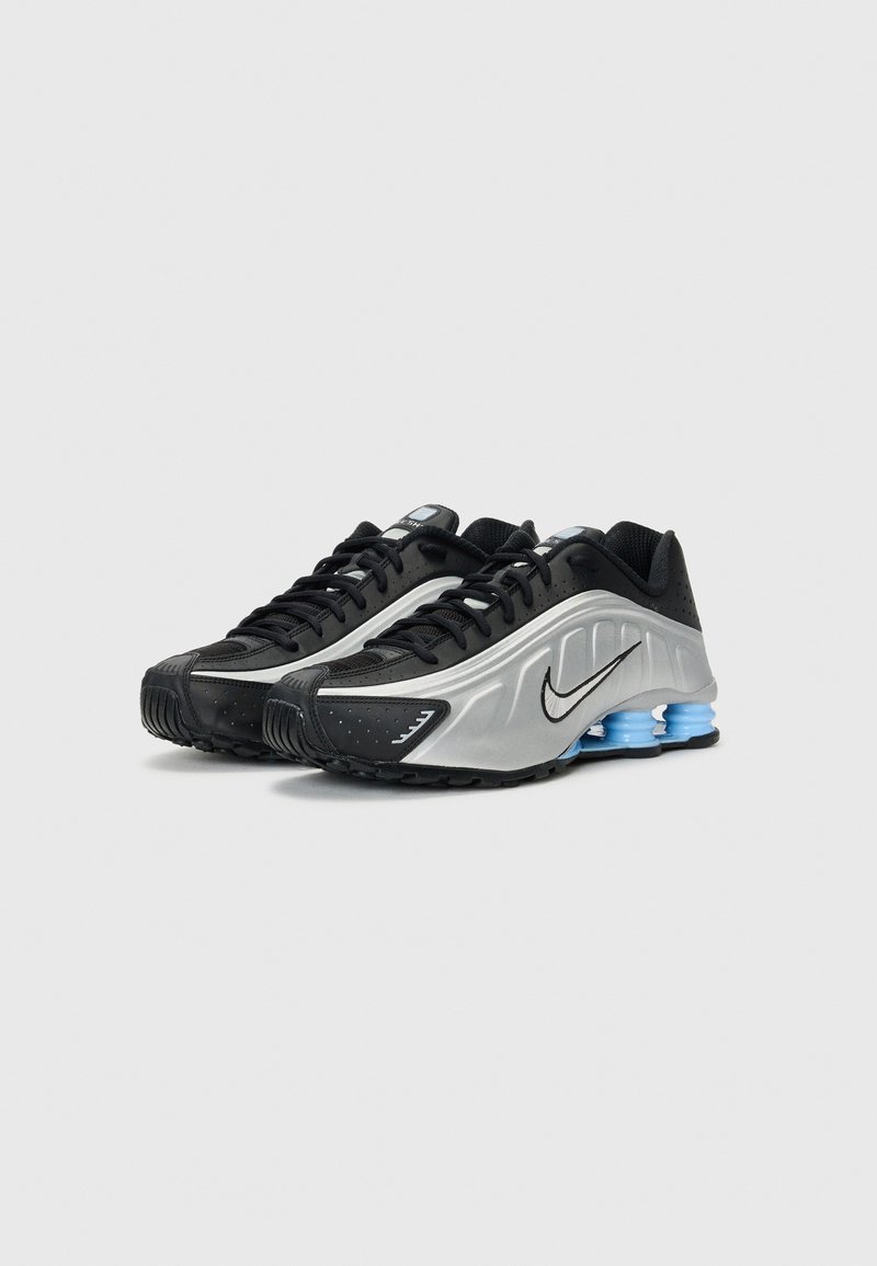 Zapatillas deportivas negras y plateadas con un diseño elegante, punta redonda, parte superior texturizada y acentos de amortiguación azul en la suela.