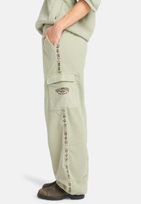 Lichtgroene fleece broek met een rechte pijp, voorzien van zijzakken en een geborduurd logo. De zijstreep bevat geometrische patronen.