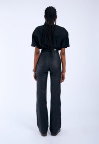 Svart oversized t-shirt med korta, vida ärmar, parat med högmidjade, utställda svarta byxor. Slät tyg med bakfickor och diskret sömnad.