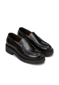 Mocassins en cuir noir avec un bout arrondi, des coutures surélevées et une épaisse semelle en caoutchouc. Nom de la marque "Marc O’Polo" embossé sur le côté.