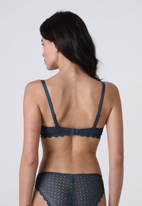 Reggiseno in pizzo teal con bordi scallop e spalline regolabili. Slip coordinato in pizzo con motivi geometrici. Chiusura posteriore con gancio.